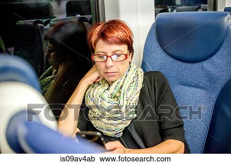 Stock Image - Mature woman reading smartphone texts whilst sitting on train. Fotosearch