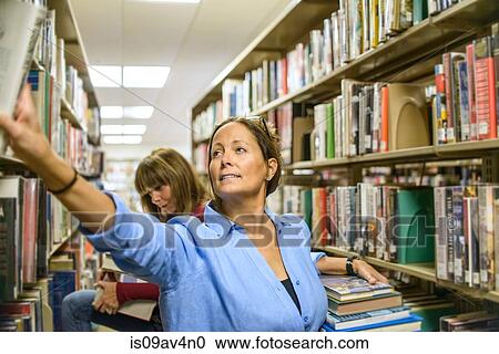 Stock Image - Mature woman searching for books in library. Fotosearch
