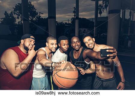 Stock Image - Men holding basketball using smartphone to take selfie. Fotosearch