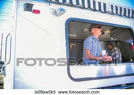 Stock Photography - Men wearing in catering van holding disposable cup looking away smiling. Fotosearch