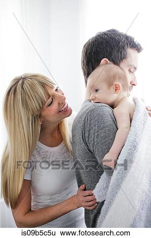 Stock Photograph - Mid adult couple carrying baby son. Fotosearch
