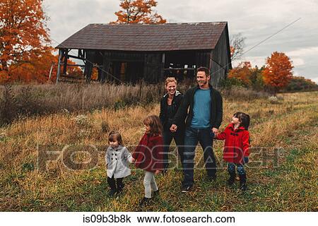 Stock Image - Mid adult family with three daughters holding hands and strolling in rural field. Fotosearch