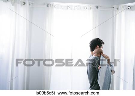 Stock Photograph - Mid adult man carrying baby son in living room. Fotosearch