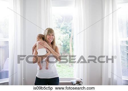 Mid adult woman carrying baby son in living room View Large Photo Image Stock Photography - Mid adult woman carrying baby son in living room. Fotosearch