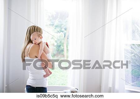 Mid adult woman carrying baby son in living room View Large Photo Image Stock Photography - Mid adult woman carrying baby son in living room. Fotosearch