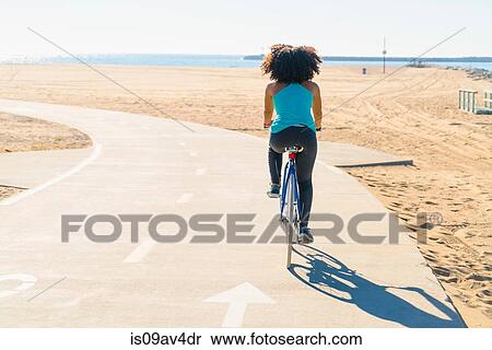 Mid adult woman cycling on pathway at beach, rear view View Large Photo Image Stock Photography - Mid adult woman cycling on pathway at beach, rear view. Fotosearch