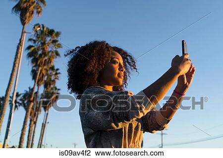 Mid adult woman, facing sunlight, taking photograph, using smartphone View Large Photo Image Stock Image - Mid adult woman, facing sunlight, taking photograph, using smartphone. Fotosearch