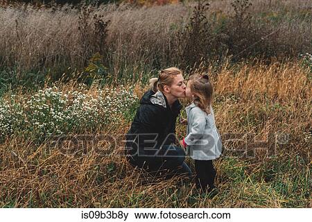 Stock Photo - Mid adult woman kissing toddler daughter in field of long grass. Fotosearch