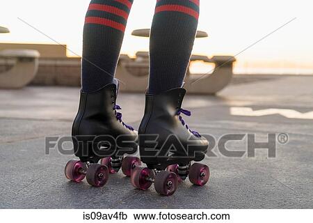 Stock Image - Mid adult woman on rollerskates, rear view, low section. Fotosearch