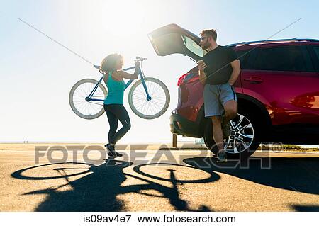 Stock Photo - Mid adult woman putting bicycle into car boot. Fotosearch