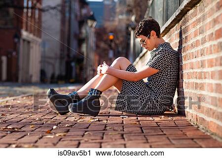 Mid adult woman sitting against brick wall View Large Photo Image Stock Image - Mid adult woman sitting against brick wall. Fotosearch