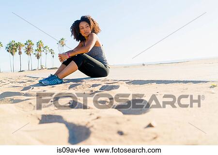 Mid adult woman sitting on beach, holding water bottle View Large Photo Image Stock Image - Mid adult woman sitting on beach, holding water bottle. Fotosearch