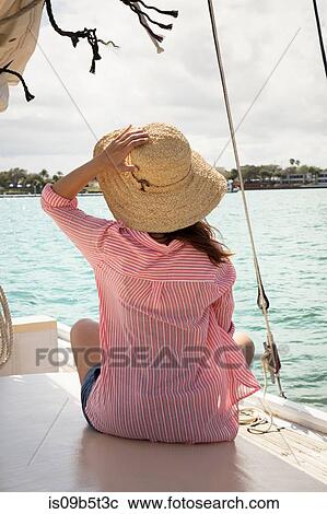 Mid adult woman sitting on deck of sailing boat, holding onto hat, rear view View Large Photo Image Stock Image - Mid adult woman sitting on deck of sailing boat, holding onto hat, rear view. Fotosearch