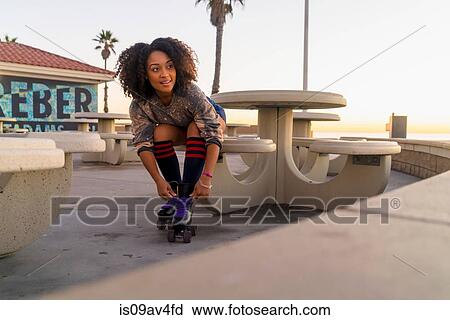 Stock Image - Mid adult woman sitting outdoors, tying rollerskates. Fotosearch