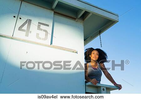 Stock Image - Mid adult woman standing on look out tower at beach, looking at view. Fotosearch
