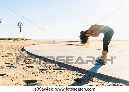 Mid adult woman standing on pathway at beach, bending over, fixing hair View Large Photo Image Stock Image - Mid adult woman standing on pathway at beach, bending over, fixing hair. Fotosearch