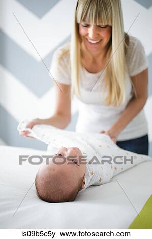 Mid adult woman swaddling baby son on bed View Large Photo Image Stock Photo - Mid adult woman swaddling baby son on bed. Fotosearch