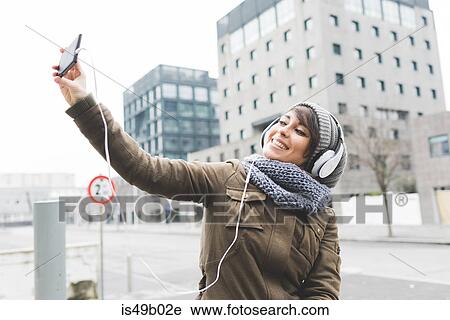 Stock Image - Mid adult woman taking smartphone selfie in city. Fotosearch