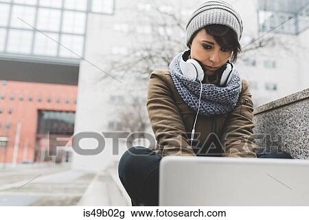 Stock Image - Mid adult woman typing on laptop in city. Fotosearch