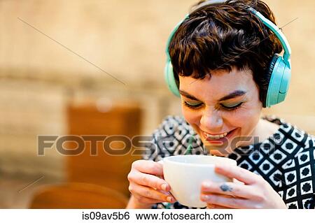 Mid adult woman, wearing headphones, holding coffee cup, smiling View Large Photo Image Stock Photograph - Mid adult woman, wearing headphones, holding coffee cup, smiling. Fotosearch