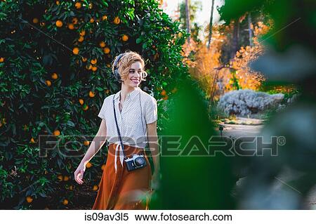 Stock Photography - Mid adult woman wearing headphones, outdoors, smiling. Fotosearch