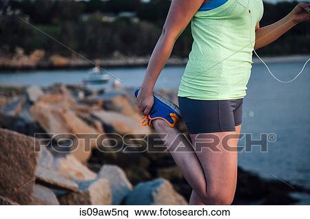 Stock Photography - Mid section of woman wearing sports clothing holding foot stretching leg. Fotosearch