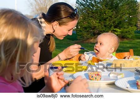 Mother and children sitting outdoors, mother feeding baby girl birthday cake View Large Photo Image Stock Image - Mother and children sitting outdoors, mother feeding baby girl birthday cake. Fotosearch