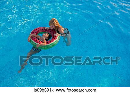 Stock Image - Mother and daughter holding onto inflatable ring in swimming pool. Fotosearch