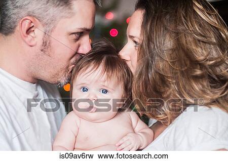 Mother and father face to face holding baby girl, kissing on head View Large Photo Image Stock Photo - Mother and father face to face holding baby girl, kissing on head. Fotosearch