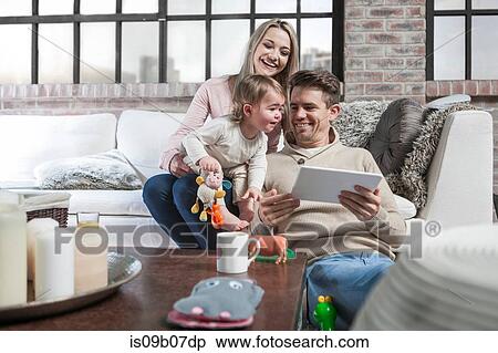 Mother and toddler sitting on sofa, toddler peering over at father's digital tablet View Large Photo Image Stock Photography - Mother and toddler sitting on sofa, toddler peering over at father's digital tablet. Fotosearch