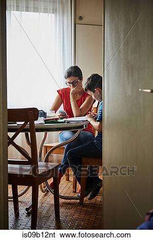Stock Photograph - Mother at dining table helping son with homework. Fotosearch