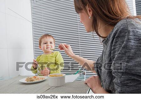 Mother feeding son at dining table View Large Photo Image Stock Photo - Mother feeding son at dining table. Fotosearch