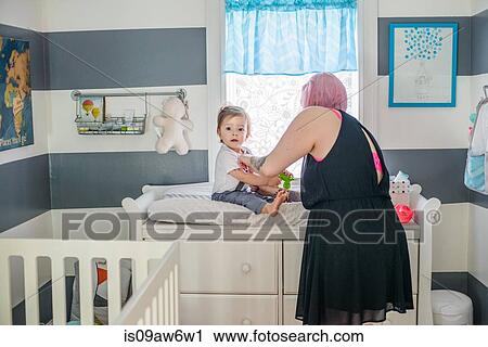 Mother getting baby son dressed on nursery day bed View Large Photo Image Stock Image - Mother getting baby son dressed on nursery day bed. Fotosearch