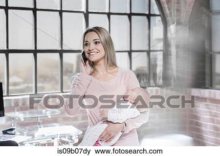 Mother holding baby daughter whilst using smartphone View Large Photo Image Stock Photo - Mother holding baby daughter whilst using smartphone. Fotosearch