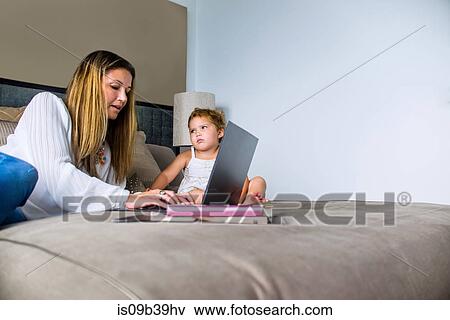 Stock Photo - Mother using laptop on bed with daughter. Fotosearch