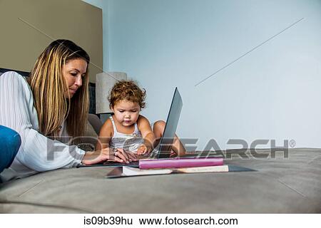 Mother using laptop on bed with daughter View Large Photo Image Stock Photograph - Mother using laptop on bed with daughter. Fotosearch