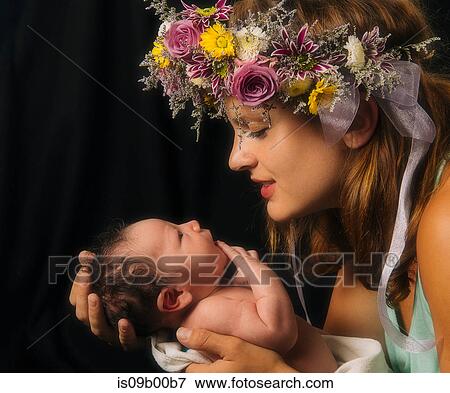 Stock Photo - Mother with flowers in hair, holding baby boy, face to face. Fotosearch