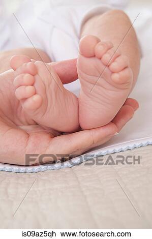 Stock Image - Mothers hand holding baby boys feet. Fotosearch