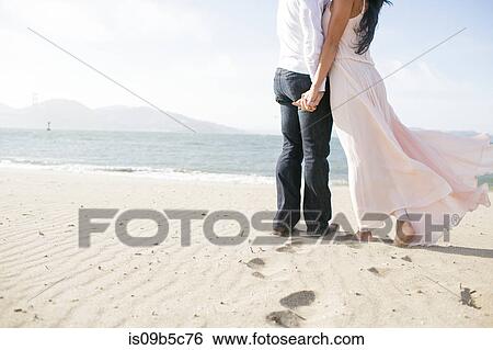 Neck down view of romantic couple hand in hand on beach View Large Photo Image Stock Photograph - Neck down view of romantic couple hand in hand on beach. Fotosearch