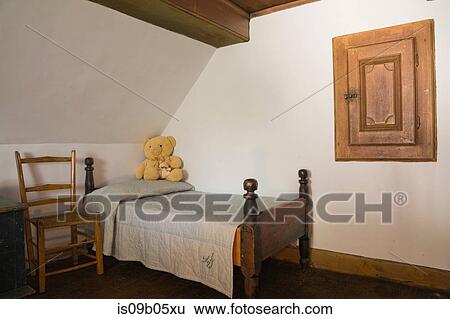 Stock Photograph - Old wooden chair and single bed in a bedroom in old (1785) fieldstone cottage style residential home, Quebec, Canada. Fotosearch
