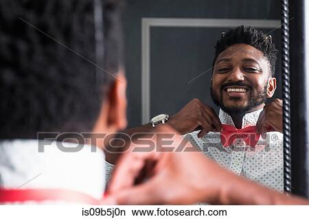 Over shoulder view of happy young businessman fastening red bow tie in mirror View Large Photo Image Picture - Over shoulder view of happy young businessman fastening red bow tie in mirror. Fotosearch