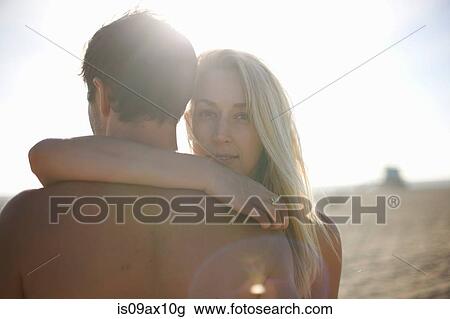 Stock Image - Over shoulder view of woman looking at camera, arm around man. Fotosearch