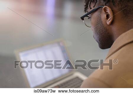 Over shoulder view of young businessman sitting in train station using laptop View Large Photo Image Stock Photo - Over shoulder view of young businessman sitting in train station using laptop. Fotosearch