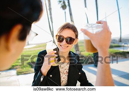Stock Image - Over shoulder view of young couple raising a juice and coffee toast, Venice Beach, California, USA. Fotosearch