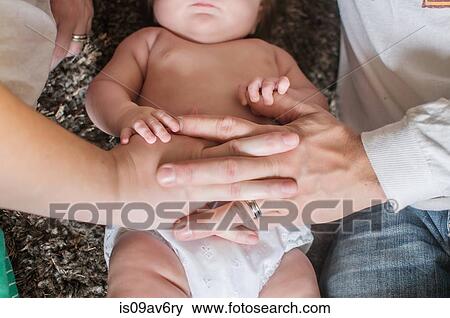 Stock Photo - Overhead cropped view of mother and fathers hand on baby girls stomach. Fotosearch