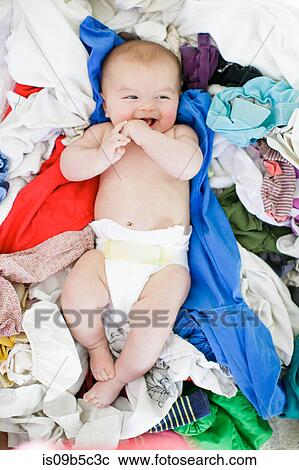 Stock Image - Overhead portrait of baby girl lying amongst laundry. Fotosearch