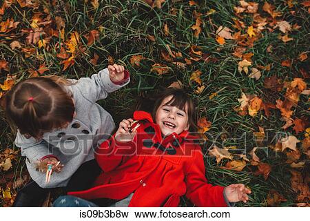 Overhead portrait of girl and toddler sister lying on grass and autumn leaves View Large Photo Image Stock Photo - Overhead portrait of girl and toddler sister lying on grass and autumn leaves. Fotosearch