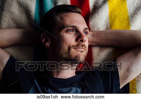 Stock Image - Overhead portrait of handsome man lying on striped blanket with hands behind head. Fotosearch