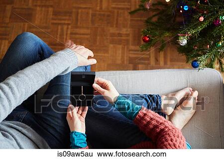 Stock Photograph - Overhead view of couple holding xmas necklace gift on living room sofa. Fotosearch