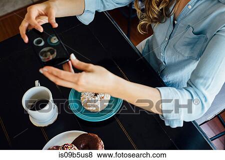 Stock Photo - Overhead view of woman photographing doughnut hole and coffee on table. Fotosearch